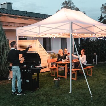 Friends celebrate a barbecue and garden party under the garden tent. The garden tent is festively decorated with fairy lights.