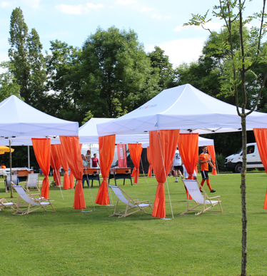 White Ecotent® 6x4 m pop-up gazebo with orange decorative curtains at an outdoor event with deck chairs.